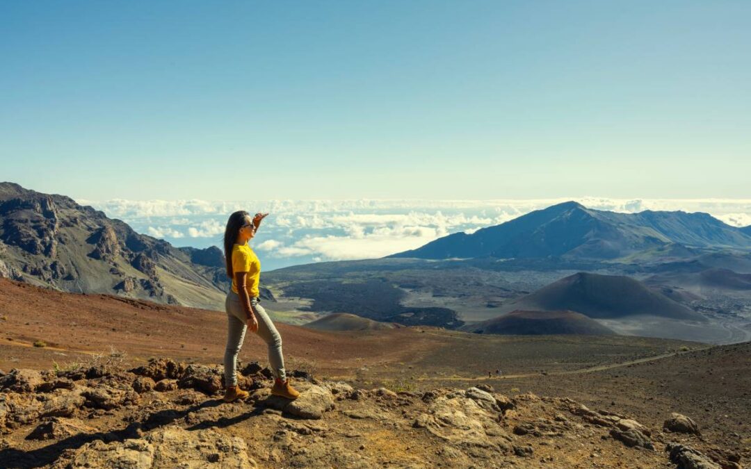 Woman standing on the view point Haleakala volcano mountain on sunrise over clouds sky background Hawaii USA.